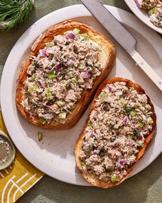 two pieces of bread with tuna salad on them next to a knife and spoons