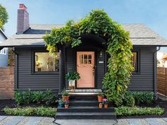 a small gray house with a pink door and some plants on the front porch,