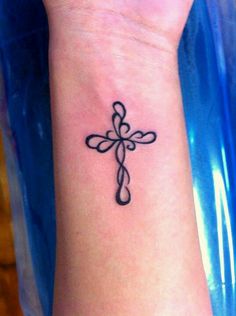 a cross tattoo on the wrist is shown in black ink, with an intricate design