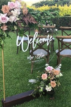 a welcome sign is set up on the grass for an outdoor ceremony with flowers and greenery