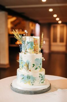 a three tiered wedding cake decorated with flowers and leaves on a white table cloth