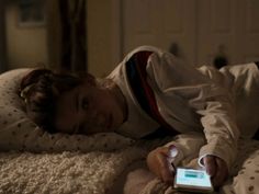 a young boy laying on top of a bed holding a cell phone in his hand