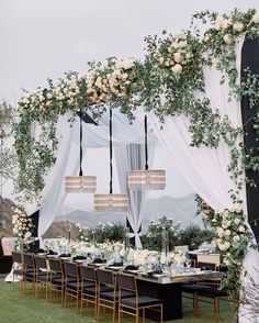 an outdoor wedding setup with white flowers and greenery on the table, hanging chandelier