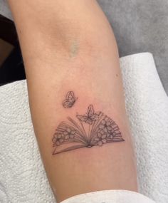 a small book tattoo with butterflies on the left arm and an open book in the middle