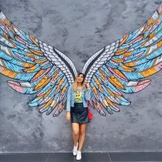 a woman standing in front of a wall with wings painted on it