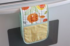 an oven mitt hanging from the side of a white stove with oranges and leaves on it