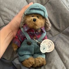 a teddy bear wearing a coat and hat on a bed with a person's hand