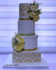 a three tiered wedding cake with yellow flowers on the top and gold trimmings