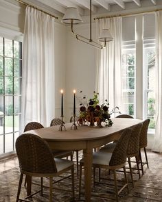 a dining room table with chairs and candles on top of it in front of large windows