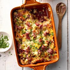 a casserole dish with meat and vegetables in it next to a wooden spoon