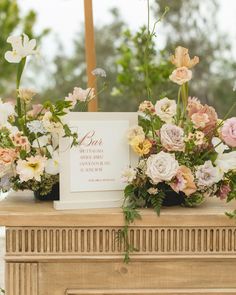 an arrangement of flowers on top of a table with a sign in the middle that says,