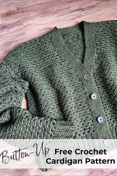 a green cardigan sweater with buttons on the front and bottom, sitting on a wooden floor