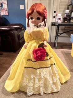 a doll with red hair wearing a yellow dress and holding a flower in her hand