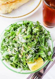 a green salad with lemon wedges and parmesan cheese on top, next to a glass of tea