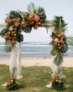 an arch decorated with flowers and greenery on the beach