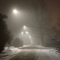 a foggy road with street lights and signs in the distance at night time,