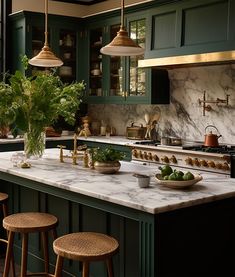 a kitchen with green cabinets and marble counter tops, hanging lights over the island area