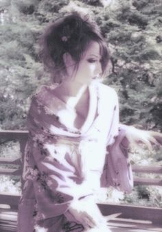 a woman in a kimono is sitting on a park bench and posing for the camera