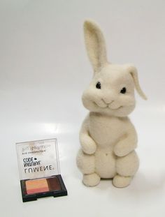 a white stuffed rabbit sitting next to a small box of makeup on a white surface