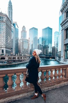 a woman standing on the side of a bridge in front of some buildings and water