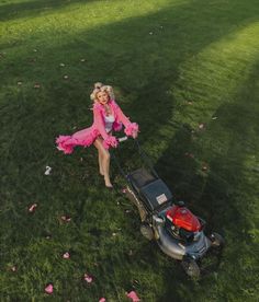 a woman in pink is pushing a lawn mower on the grass with flowers all around her