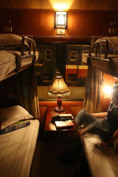 bunk beds in a train car with two people sitting on the floor and one person reading