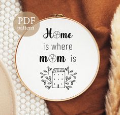 a cross - stitch pattern with the words home is where mom is on it and an orange blanket next to it