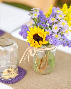 a mason jar filled with purple and yellow flowers on top of a white table cloth