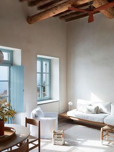 a living room filled with white furniture and wooden beams on the ceiling next to windows