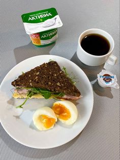 a white plate topped with an egg and sandwich next to a cup of black coffee