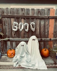 two halloween pumpkins sitting on the ground in front of a wooden fence with balloons