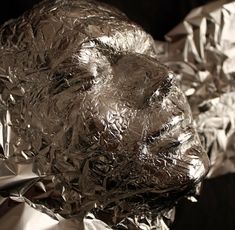 an animal made out of aluminum foil sitting on top of a black surface with its head covered in tinfoil