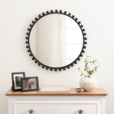 a white dresser topped with a mirror and a vase filled with flowers next to it