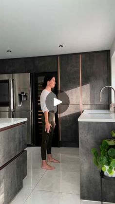 a woman standing in the middle of a kitchen with an open refrigerator and sink area