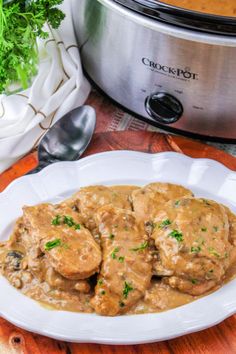 a white plate topped with meat and gravy next to a crock pot