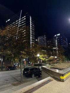 a black car parked on the side of a road next to tall buildings at night