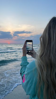 a woman taking a photo with her cell phone on the beach at sunset or sunrise