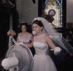 two women in wedding dresses standing next to each other with a fan on their shoulder