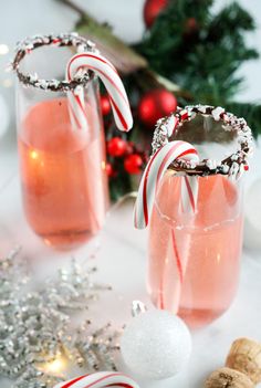 two glasses filled with pink liquid and candy canes next to christmas decorations on a table