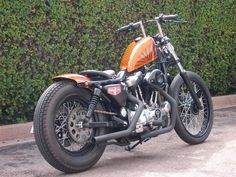 an orange and black motorcycle parked in front of a hedge