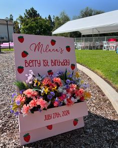 a sign with flowers and strawberries on it in front of a tent at a birthday party