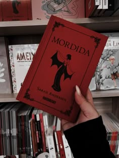 a person holding up a red book in front of a bookshelf full of books