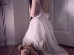 a woman in a white dress sitting on the floor next to a teddy bear