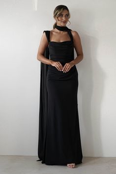 a woman in a black dress standing next to a wall with her hands on her hips