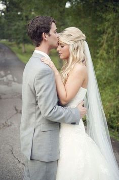 a bride and groom standing on the side of a country road in front of trees