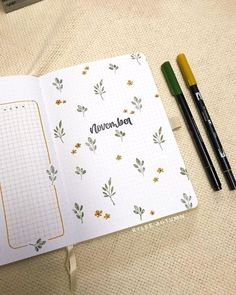 an open notebook sitting on top of a bed next to two pens