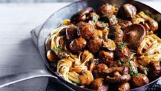 a skillet filled with pasta and meat covered in sauce on top of a wooden table