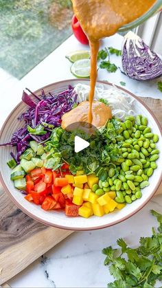 a bowl filled with vegetables and dressing being drizzled on top of it