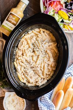 pasta in a crock pot with bread and salad behind it