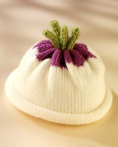 a white knitted hat with a purple and green flower on it's brim